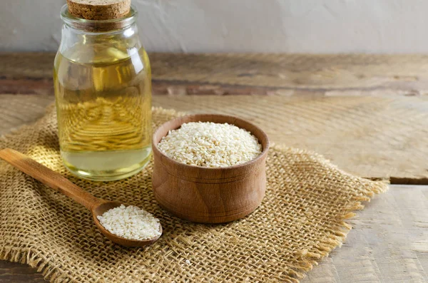 Sesame oil in glass jar with seeds in wooden bowl and spoon on wooden table. Concept of healthy eating. Horizontal orientation. Copy space.