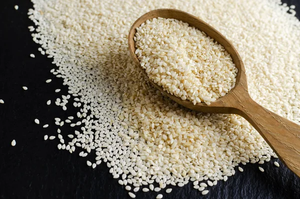 Wooden spoon with sesame seeds scattered on a black background. Concept of healthy food. Horizontal orientation