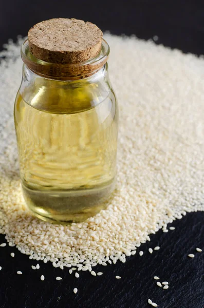 Sesame oil in glass jar with seeds on black background. Concept of healthy eating. Vertical orientation.