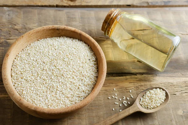 Sesame oil in glass jar with seeds in wooden bowl and spoon on wooden table. Concept of healthy eating. Horizontal orientation.