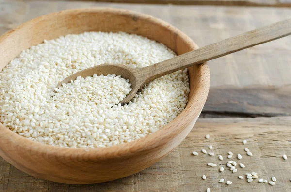 Sesame seeds in a wooden bowl with a spoon on a wooden table. Concept of healthy eating. Horizontal orientation.