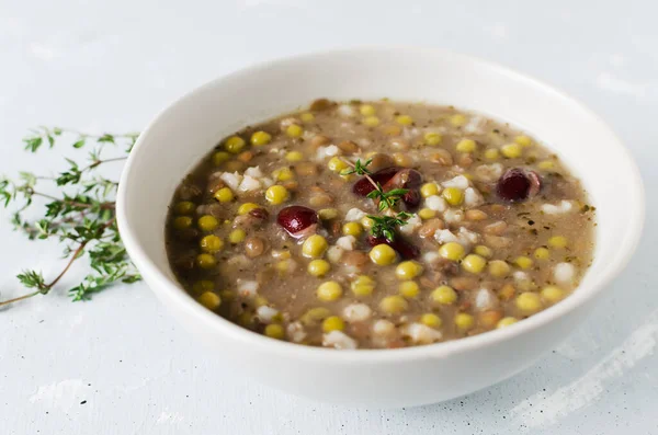 Bean soup in a ceramic gray bowl with a sprig of thyme and a piece of bread on a wooden table. A mix of red beans, lentils and peas. The concept of vegetarian food. Horizontal orientation.