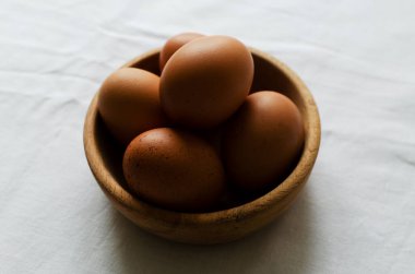 Beyaz bir masa örtüsü üzerinde ahşap bir kasede tavuk yumurtası. Kırsal tarzda. Organik gıda kavramı. Arka ışık. Yatay yönelim.