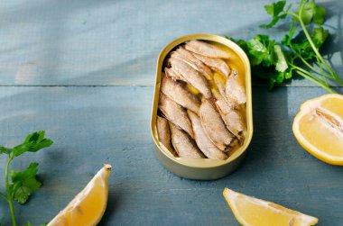 Mavi ahşap bir masada maydanozlu ve limonlu konserve balık. Konserve balık konsepti. Yatay oryantasyon. Boşluğu kopyala.