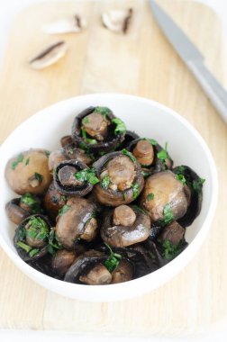 Kızarmış şampiyonlar, sarımsak ve maydanozla ahşap masada gri beyaz bir masa. Vejetaryen yemeği kavramı. Dikey oryantasyon. Seçici odak.