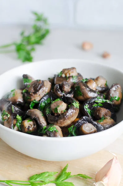 stock image Fried champignons with garlic and parsley in a gray bowl. The concept of vegetarian food. Vertical orientation. Selective focus.