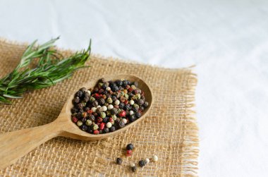 Siyah, beyaz, kırmızı ve baharatlı biberlerin karışımı. Çuval bezi üzerinde ahşap kaşıklarda ve hafif arkaplanda biberiye filizi. Kurutulmuş baharat biberi konsepti. Seçici odaklanma. Boşluğu kopyala