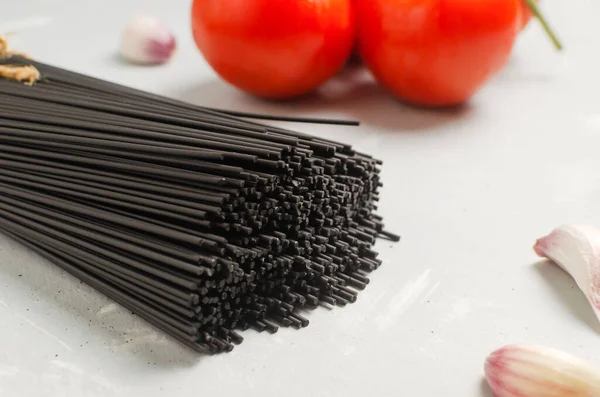 イカ墨と生黒スパゲティの束 灰色の背景にトマトとニンニク 健康的なイタリア料理の概念 水平方向 選択的フォーカス スペースのコピー — ストック写真
