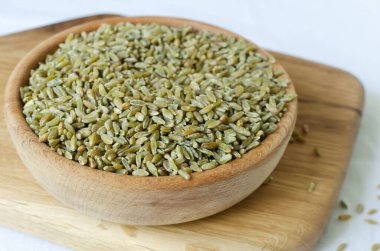Raw freekeh or firik in a wooden bowl on cutting board. Concept of healthy eating. Rustic style. Horizontal orientation. Selective focus. clipart
