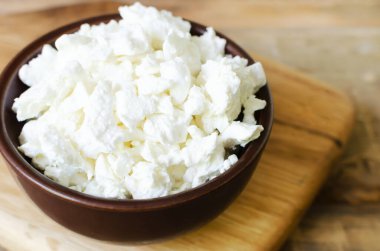 Kahverengi bir seramik kasede, ahşap bir masanın üzerinde organik süzme peynir. Ev yapımı yemek kavramı. Seçici odaklanma. Yatay yönelim.