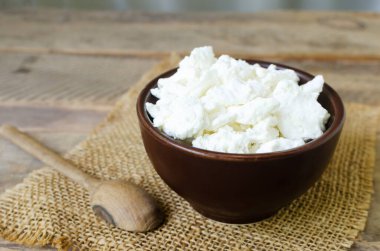 Kahverengi seramik kasede organik süzme peynir ve tahta bir arka planda çuval bezi. Ev yapımı yemek kavramı. Yatay yönelim.