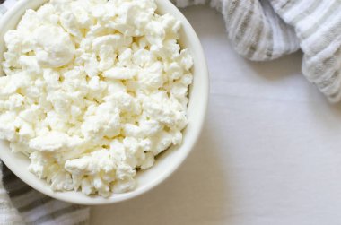 Beyaz bir seramik kasede beyaz bir masa örtüsünün üzerinde mutfak havlusu olan organik süzme peynir. Sağlıklı kahvaltı. Sağlıklı gıda kavramı. Seçici odaklanma. Yatay oryantasyon. Üst Manzara. Boşluğu kopyala.