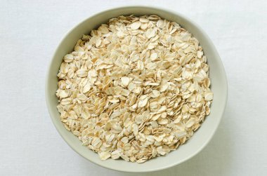 Beyaz bir masa örtüsü üzerinde gri bir kasede çiğ yulaf ezmesi. Sağlıklı kahvaltı kavramı. Vejetaryen ve vejetaryen. Yatay oryantasyon. Seçici odaklanma. Üst görünüm