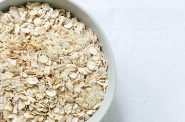 Beyaz bir masa örtüsü üzerinde gri bir kasede çiğ yulaf ezmesi. Sağlıklı gıda kavramı. Vejetaryen ve vejetaryen. Yatay oryantasyon. Seçici odaklanma. Üst görünüm