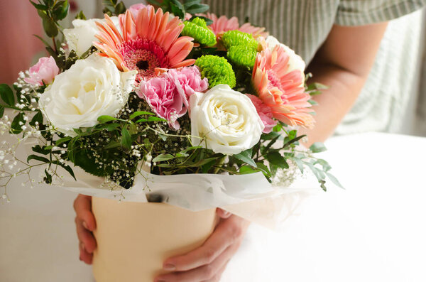 A woman holds a festive bouquet of white roses, pink gerberas and carnations. Birthday. Mother's Day. The concept of holiday flowers. Selective focus. Horizontal orientation. Copy space