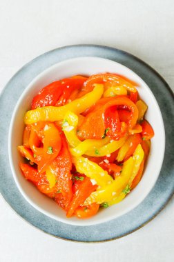 Kırmızı ve sarı kavrulmuş biber dilimleri, sarımsak ve maydanozlu gri seramik kaseli salata. Sağlıklı beslenme kavramı. Geleneksel İtalyan yemeği. Vejetaryen ve vejetaryen. Dikey oryantasyon. Üst görünüm