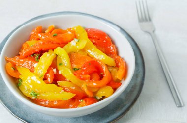 Kırmızı ve sarı biber dilimli salata, sarımsak ve maydanoz gri seramik kasede çatallı. Sağlıklı beslenme kavramı. Geleneksel İtalyan yemeği. Vejetaryen ve vejetaryen yemekleri.