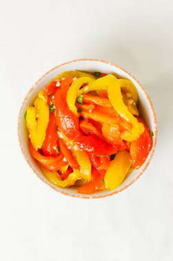 Kırmızı ve sarı kavrulmuş biber dilimleri, sarımsak ve maydanozlu beyaz seramik kasede salata. Sağlıklı beslenme kavramı. Geleneksel İtalyan yemeği. Vejetaryen ve vejetaryen yemekleri. Dikey yönelim.