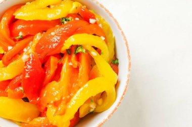 Kırmızı ve sarı kavrulmuş biber dilimleri, sarımsak ve maydanozlu beyaz seramik kasede salata. Sağlıklı beslenme kavramı. Geleneksel İtalyan yemeği. Vejetaryen ve vejetaryen yemekleri. Yatay yönelim.