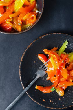 Kırmızı ve sarı kavrulmuş biber dilimleri, sarımsak ve maydanozlu siyah seramik tabakta salata. Sağlıklı beslenme kavramı. Geleneksel İtalyan yemeği. Vejetaryen ve vejetaryen yemekleri.