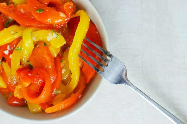 Kırmızı ve sarı biber dilimli salata, sarımsak ve maydanoz gri seramik kasede çatallı. Sağlıklı beslenme kavramı. Geleneksel İtalyan yemeği. Dikey oryantasyon. Üst görünüm