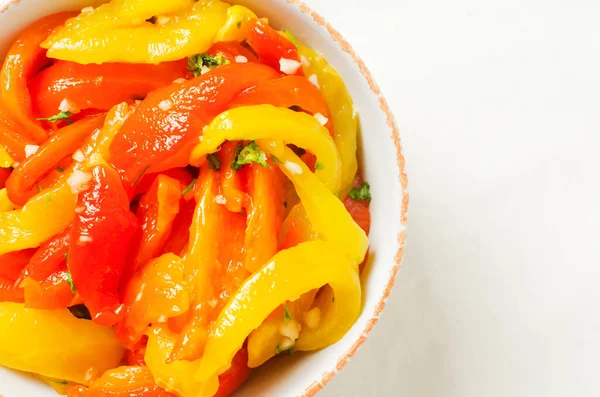 Kırmızı ve sarı kavrulmuş biber dilimleri, sarımsak ve maydanozlu beyaz seramik kasede salata. Sağlıklı beslenme kavramı. Geleneksel İtalyan yemeği. Vejetaryen ve vejetaryen yemekleri. Yatay yönelim.