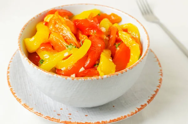Kırmızı ve sarı kavrulmuş biber dilimleri, sarımsak ve maydanozlu beyaz seramik kasede salata. Sağlıklı beslenme kavramı. Geleneksel İtalyan yemeği. Vejetaryen ve vejetaryen yemekleri. Yatay yönelim.