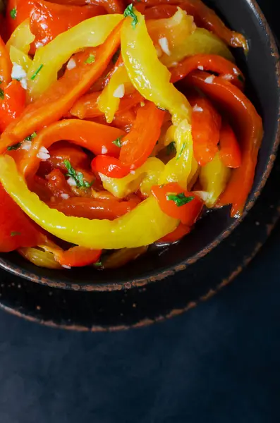 Kırmızı ve sarı kavrulmuş biber dilimleri, sarımsak ve maydanozlu salata siyah arka planda seramik kasede. Sağlıklı beslenme kavramı. Geleneksel İtalyan yemeği. Vejetaryen ve vejetaryen yemekleri.