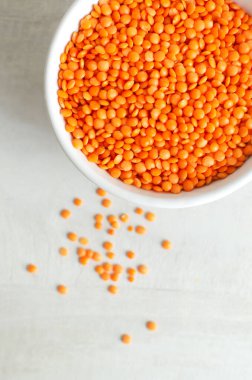 Arka planda beyaz bir kasede turuncu mercimek. Düzgün beslenme kavramı. Vejetaryen ve vejetaryen yemekleri. Dikey oryantasyon. Üst Manzara. Boşluğu kopyala.