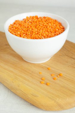 Beyaz bir kasede, arka planda tahta bir kesme tahtasının üzerinde turuncu mercimek. Düzgün beslenme kavramı. Vejetaryen ve vejetaryen yemekleri. Dikey yönelim.