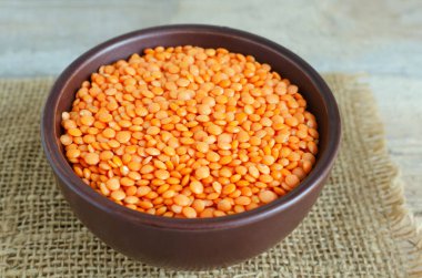 Kahverengi bir seramik kasede, tahta bir masanın üzerinde turuncu mercimek. Düzgün beslenme kavramı. Vejetaryen ve vejetaryen yemekleri. Kırsal tarzda. Yatay yönelim.