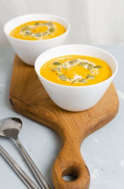 Gri arka planda tahta kesim tahtasının üzerinde kurumuş tohumlar ve kekik yapraklarıyla iki kase balkabağı kreması çorbası. Sağlıklı beslenme kavramı. Vejetaryen ve vejetaryen yemekleri. Dikey yönelim.