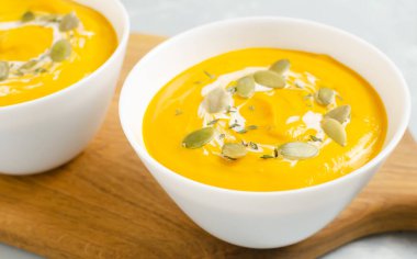 Gri arka planda tahta kesim tahtasının üzerinde kurumuş tohumlar ve kekik yapraklarıyla iki kase balkabağı kreması çorbası. Sağlıklı beslenme kavramı. Vejetaryen ve vejetaryen yemekleri. Seçici odak