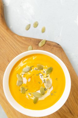 Beyaz bir kase balkabağı kremalı çorba içinde kurutulmuş tohumlar ve kekik yaprakları gri arka planda tahta bir kesim tahtasının üzerinde. Sağlıklı beslenme kavramı. Vejetaryen ve vejetaryen yemekleri. Üst Manzara. Boşluğu kopyala