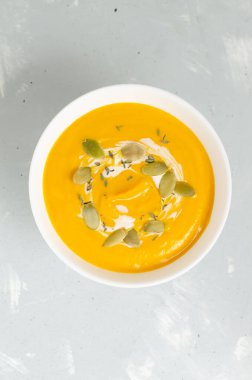 Beyaz bir kase balkabağı kremalı çorba içinde kuru tohumlar ve gri arka planda kekik yaprakları. Sağlıklı beslenme kavramı. Vejetaryen ve vejetaryen yemekleri. Dikey oryantasyon. Üst görünüm