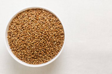 Organik kuru karabuğday, arka planda beyaz bir kasede inliyor. Vejetaryen ve vejetaryen yemekleri. Sağlıklı beslenme kavramı. Yatay oryantasyon. Üst Manzara. Boşluğu kopyala.