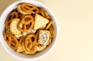 Arka planda beyaz bir kasede atıştırmalık bir şeyler. Tuzlu krakerler, çeşitli şekillerde krakerler ve tohumlarla. Fast food. Zararlı atıştırmalık. Yatay oryantasyon. Üst Manzara. Boşluğu kopyala