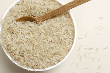 Beyaz kâse içinde çiğ basmati pilavı ve arka planda tahta kaşık. Su tasarrufu ürünleri kavramı. Su tasarrufu. Vejetaryen ve vejetaryen yemekleri. Yatay oryantasyon. Üst Manzara. Boşluğu kopyala