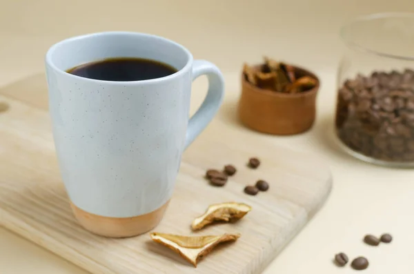 Mushroom coffee in a blue cup with dried mushrooms on a wooden cutting board on a yellow background. The concept of a trendy beverage. The drink is good for health. Selective focus.