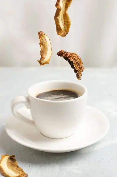 Mushroom coffee in a white cup and saucer with dried mushrooms and coffee beans. The concept of a trendy beverage. The drink is good for health. Vertical orientation. Selective focus. Flying food