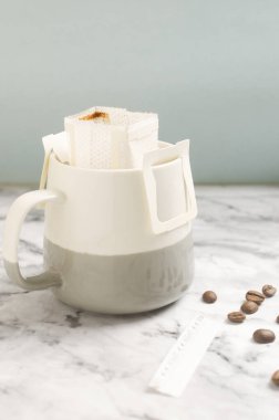Kahve poşetini gri mermer arka planda bir fincana boşalt. Lezzetli ve aromatik bir içki hazırlamanın hızlı bir yolu. Dikey oryantasyon. Seçici odak