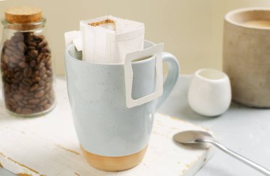 Bir poşet kahveyi gri arka planda bir fincana dökme işlemi. Lezzetli ve aromatik bir içki hazırlamanın hızlı bir yolu. Yatay oryantasyon. Seçici odak