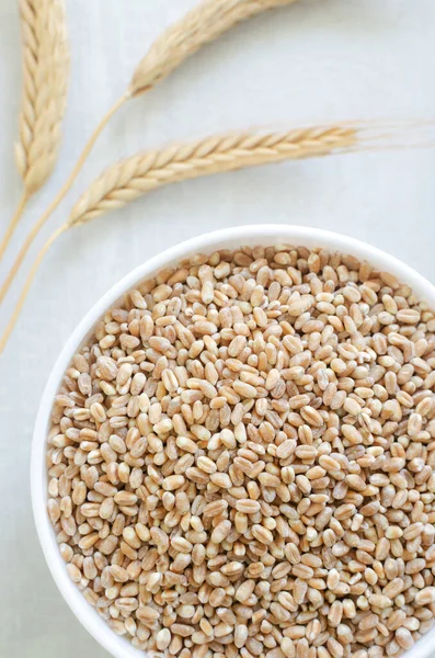 Wheat groats in a white bowl with three ears of wheat on a light background. Rustic style. Concept of healthy food. Vertical orientation. Top view