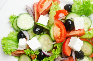 Beyaz ahşap bir masada salatalık, domates, kırmızı soğan, feta peyniri, marul ve siyah zeytinli klasik Yunan salatası. Geleneksel yemek kavramı. Basit malzemeler. Üst görünüm.