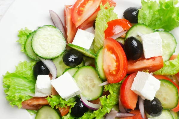 Beyaz ahşap bir masada salatalık, domates, kırmızı soğan, feta peyniri, marul ve siyah zeytinli klasik Yunan salatası. Geleneksel yemek kavramı. Basit malzemeler. Üst görünüm.