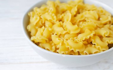 Beyaz tahta bir tahtanın üzerinde gri bir kasede çiğ Creste Di Gallo makarnası. Horoz tarağı. Geleneksel İtalyan yemeği kavramı. Yatay oryantasyon. Uzayı kopyala Seçici odak