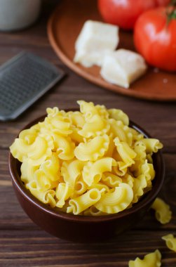 Çiğ Creste Di Gallo makarnası seramik bir kasede taze domates ve parmesan peyniri ile kahverengi tahta üzerinde. Horoz tarağı. Geleneksel İtalyan mutfağı kavramı. Dikey yönelim.