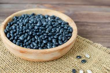 Tahta bir masada çuval bezi üzerinde tahta bir kasede çiğ siyah bens. Kırsal tarzda. Vejetaryen gıda konsepti. Yatay oryantasyon. Seçici odak.