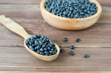 Tahta kaşıkta çiğ siyah bens ve tahta masada bowling. Kırsal tarzda. Vejetaryen gıda konsepti. Yatay oryantasyon. Seçici odak.