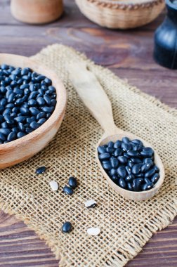 Tahta bir kaşıkta çiğ siyah bens ve tahta bir masada çuval bezi üzerinde bowling. Kırsal tarzda. Sağlıklı beslenme kavramı. Dikey oryantasyon. Seçici odak.